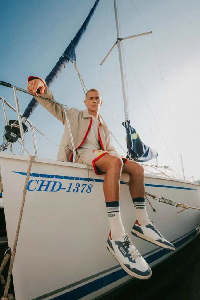 Jovem em veleiro, casaco riscas, calções, sapatilhas estilo.