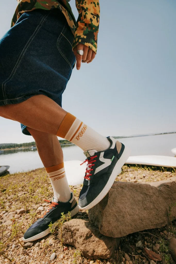 Pessoa com ténis, meias 1985 e calções jeans junto ao lago.