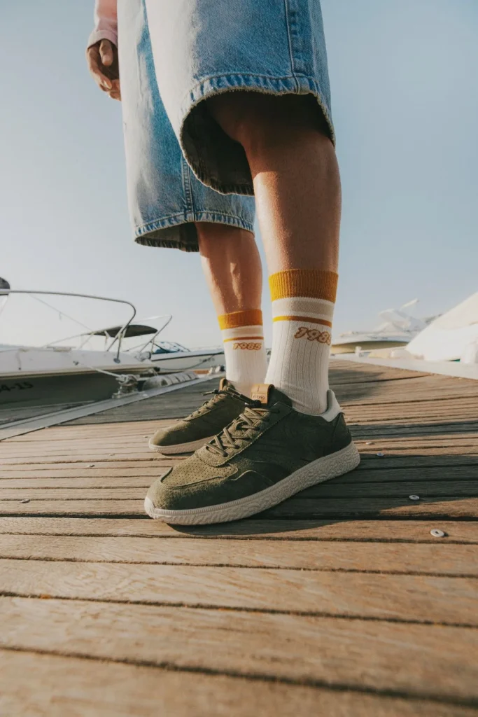 Homem com ténis verdes, meias, calções de ganga em cais.