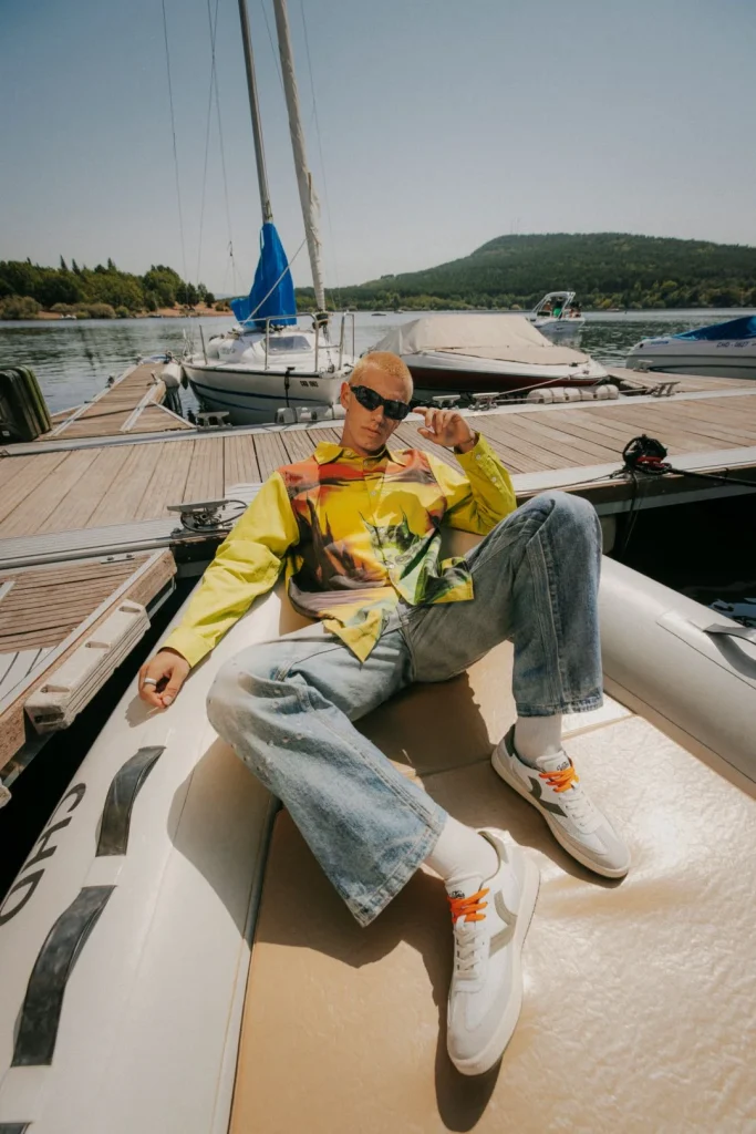 Jovem estiloso em barco, com camisa vibrante e óculos de sol.