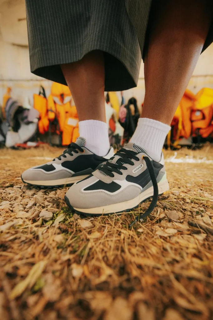 Pés com sapatilhas pretas e cinzentas sobre chão de terra.