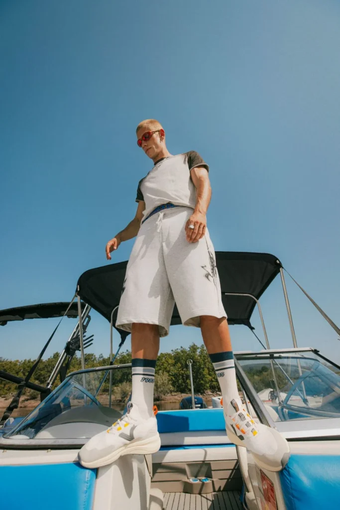 Homem loiro com óculos vermelhos e roupa casual em barco.