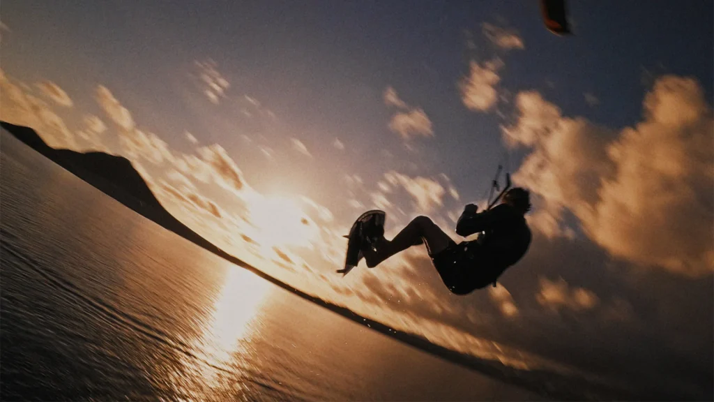 Atleta a praticar kitesurf com um salto de grande altitude ao pôr do sol nas Ilhas Canárias para ilustrar a procura constante de adrenalina