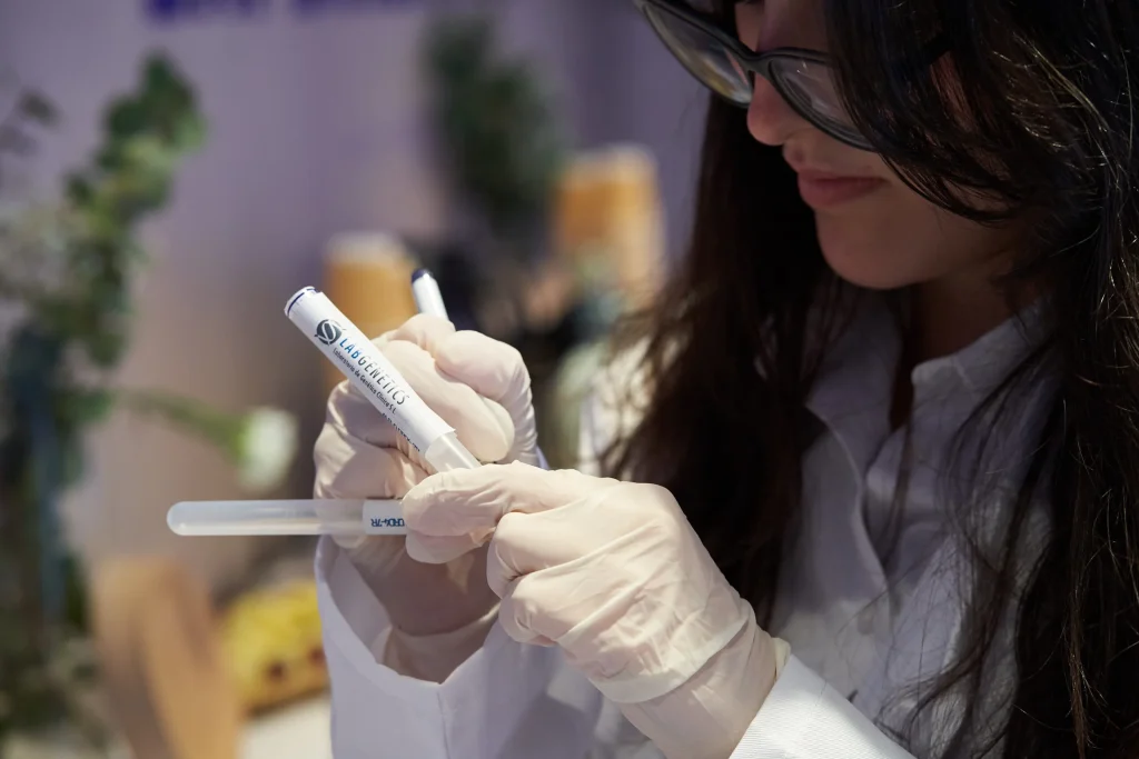 Especialista de laboratório a manusear cuidadosamente um tubo de recolha de saliva com a inscrição DRD4-7R para detetar a variante genética da exploração