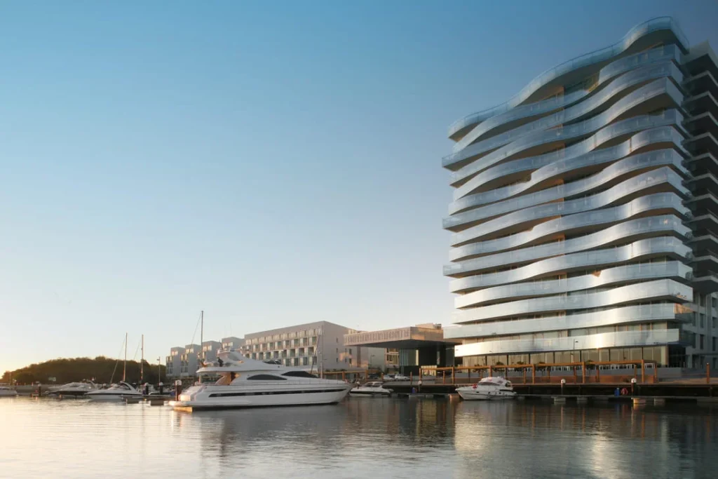 Edifício moderno com varandas onduladas frente a uma marina.