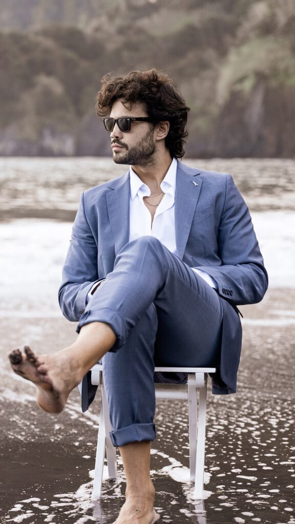 Homem elegante de fato sentado na praia.