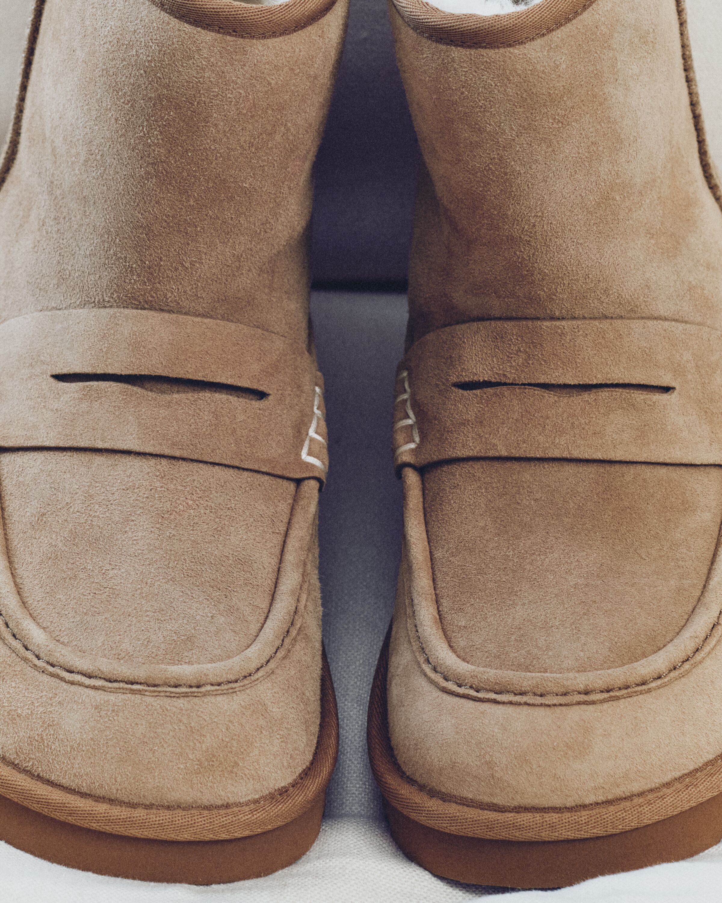 Detalhe frontal das botas UGG JW Anderson Loafer em camurça castanha com tira estilo penny loafer e costuras brancas