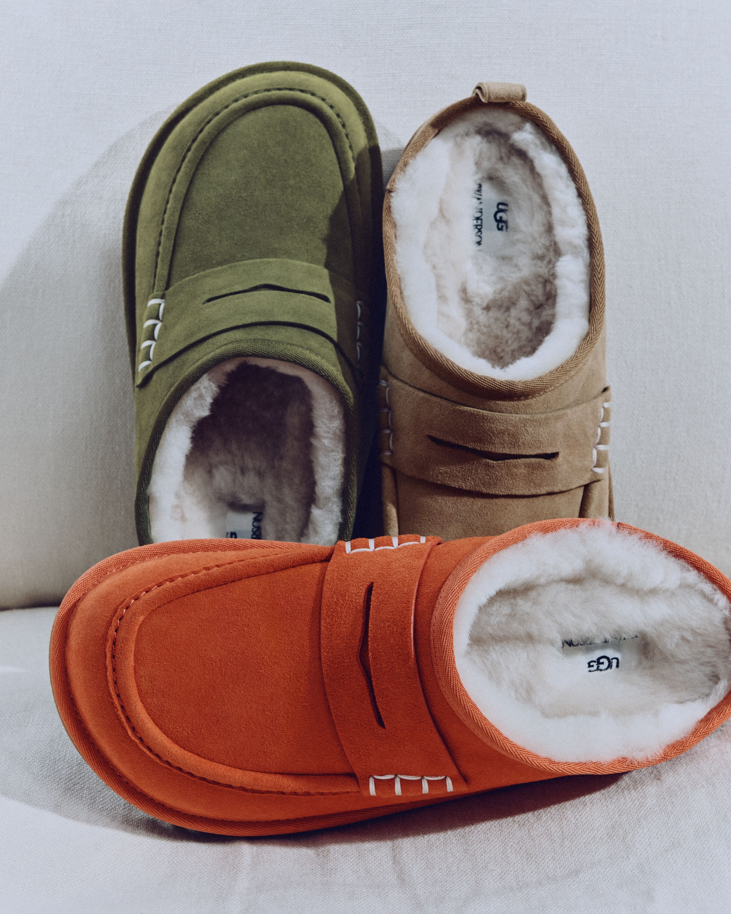 Três sapatos UGG JW Anderson Loafer em camurça nas cores verde, bege e laranja com costuras brancas e interior forrado a pelo
