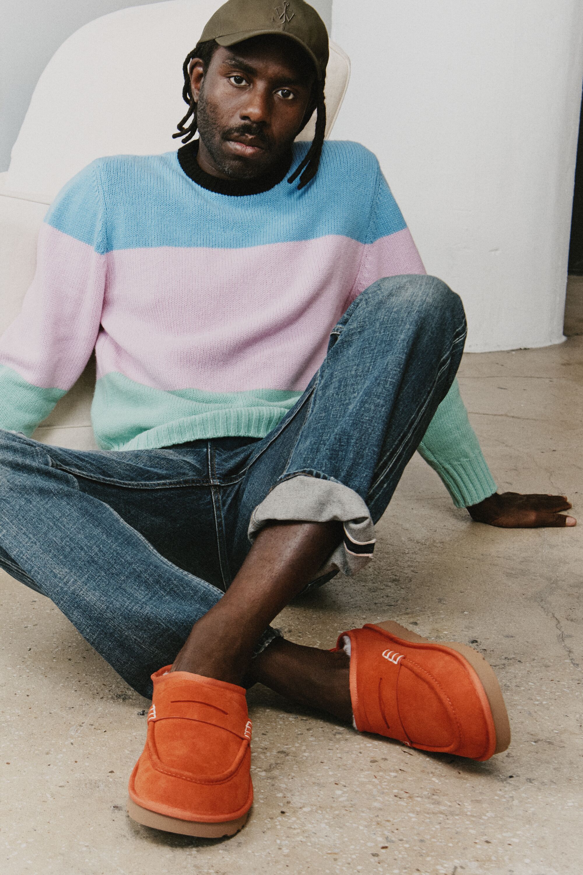 Homem sentado no chão a usar os sapatos cor-de-laranja UGG JW Anderson Loafer com calças de ganga e camisola