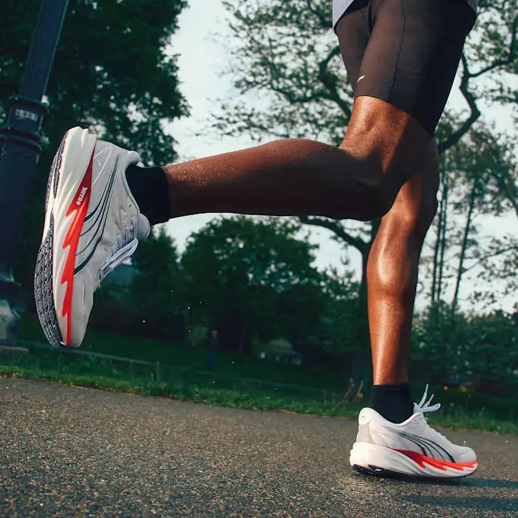 Pessoa a correr com ténis Puma brancos e laranja.