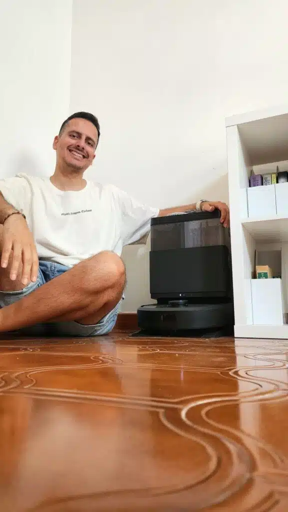 Pessoa sentada ao lado de robô aspirador preto.