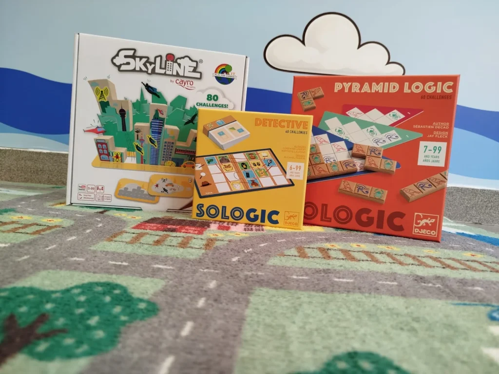 Três caixas de jogos de lógica sobre um tapete infantil.