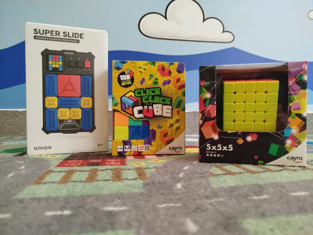 Três puzzles em embalagens originais sobre um tapete infantil.