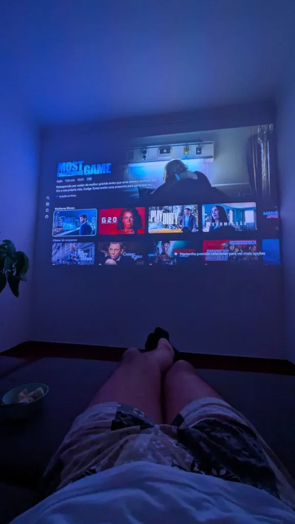 Pessoa a ver filmes projetados na parede de um quarto.