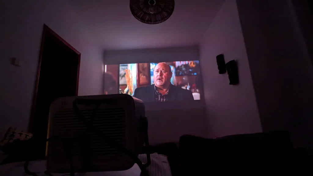 Projetor portátil a exibir filme numa parede em sala escura.