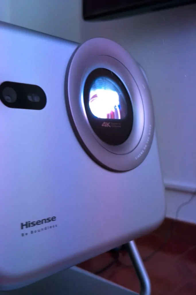 Projetor Hisense 4K prateado em funcionamento com lente iluminada.