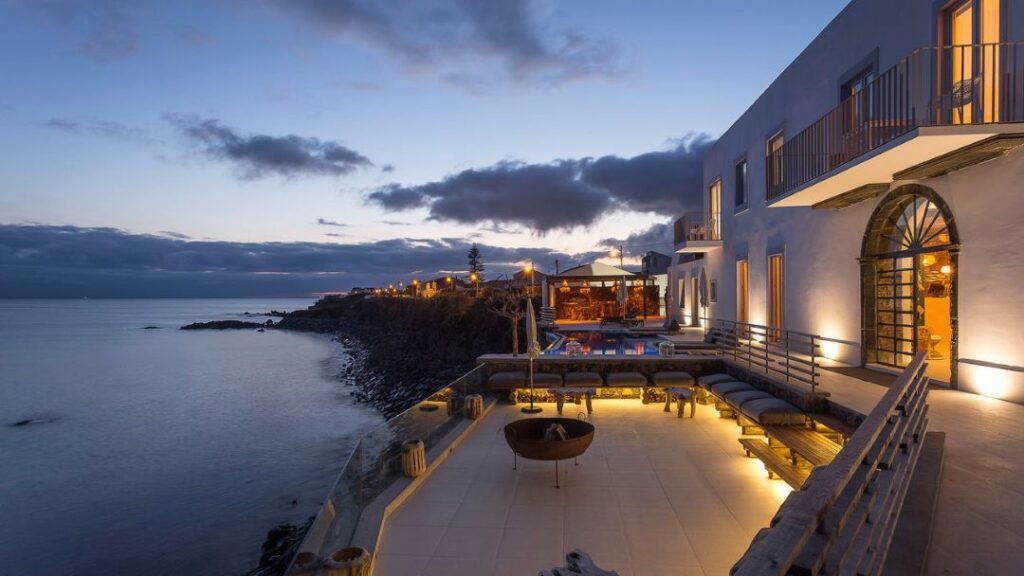 Hotel à beira-mar ao anoitecer, iluminação acolhedora.